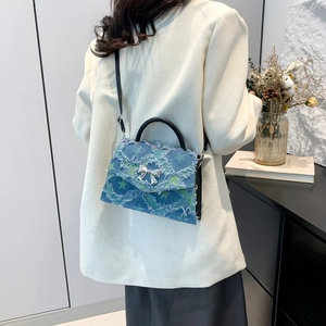 Blue denim crossbody bag with green star print and silver bow buckle shown on a model