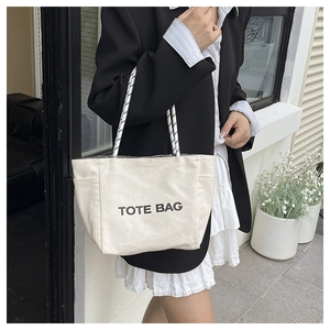 Detail view of large white canvas tote bag with black letter print and braided rope strap