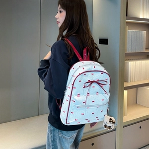 Detail of white backpack with red bow prints and plush kitten charm in cozy library setting