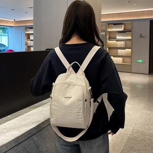 Nahaufnahme des beigen Nylon-Rucksacks mit Doppelreißverschluss und Metall-Markenplakette