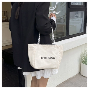Detailed view of cream canvas tote bag with letter print and black and white woven handles