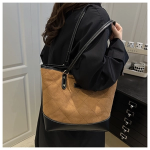 Detail of a large brown quilted suede tote bag with black leather straps on shoulder