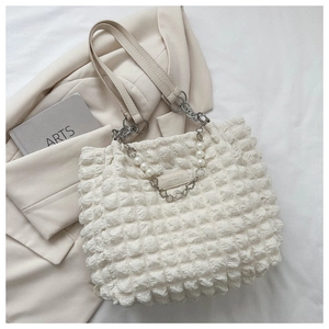 Detail van witte tas met bubbeltextuur, zilveren ketting en bloemige metalen gespen