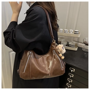Brown leather hobo bag featuring silver zippers with long tassels and a plush ball pendant