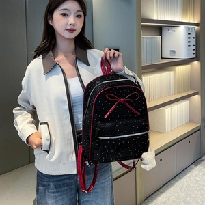 Detail of black polka dot backpack with a large red bow and cute plush bear charm