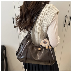 Detail view of large dark brown leather shoulder bag with silver zippers and lion charm