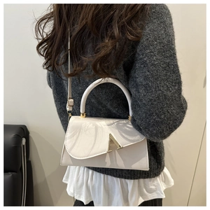 Detail of a creamy white crossbody bag showing the elegant gold A-shaped metal clasp