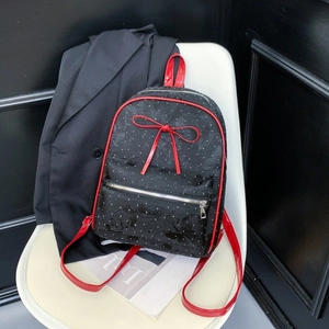 Detail of black backpack with red bow, white polka dots, and silver metal zippers