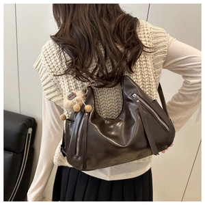 Detail of dark brown tote bag featuring silver zippers with long tassels and plush charm