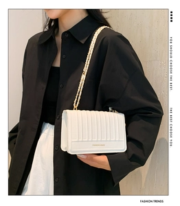 Detail view of white chain strap bag with vertical quilted texture and metal hardware