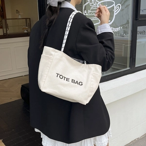 Large capacity off-white canvas tote bag with letter print shown on model at a cafe