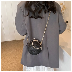 Chic black spherical evening bag with glitter finish and gold ring handle worn by model