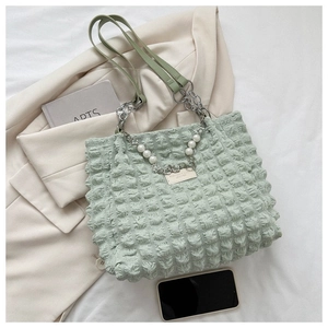 Detail van lichtgroene tote bag met bubbeltextuur, parelketting en leren riemen