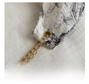 Dettaglio del tessuto floreale in peluche bianco con occhielli e catena dorata
