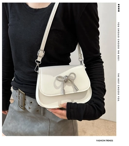 Close-up of a white leather saddle bag with a sparkling rhinestone bow buckle and strap