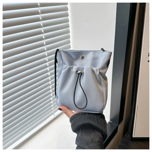 Detail van een lichtblauwe oxford crossbodytas met trekkoordzak en metalen magneetsluiting