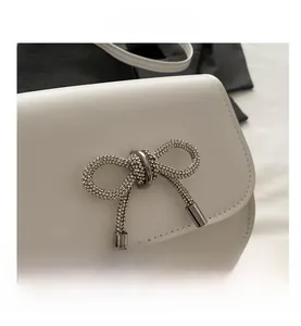 Detail of a white leather saddle bag featuring a sparkling rhinestone bow buckle design