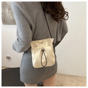 Crèmewitte crossbodytas gedragen door model met verstelbaar koordzakje en minimalistische stijl