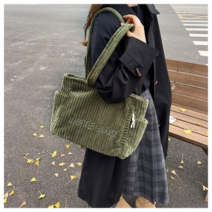Close-up of dark green corduroy tote bag with embroidered letters and side pocket