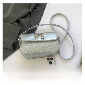 Detail der silbernen Tweed-Umhängetasche mit Metallschleife und Handy zum Größenvergleich