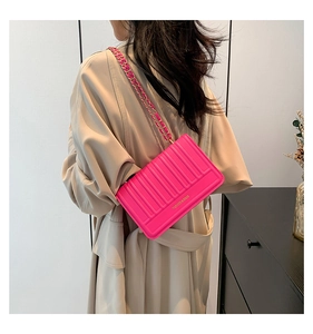 Détail d'un sac à bandoulière matelassé rose vif avec chaîne porté sur un trench-coat beige