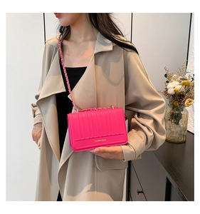 Gros plan d'un sac à bandoulière rose magenta porté avec un trench-coat beige