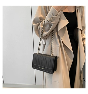 Detail of black quilted chain crossbody bag showing vertical stitching and gold metal strap