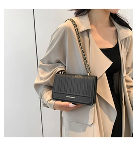 Détail du sac bandoulière plissé noir avec chaîne et logo doré sur un trench-coat