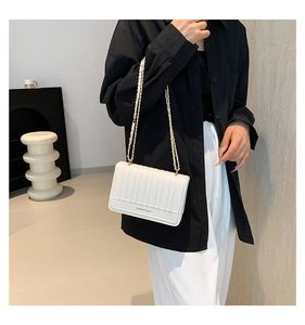 Detail of white quilted chain crossbody bag with vertical stitching and gold-tone strap