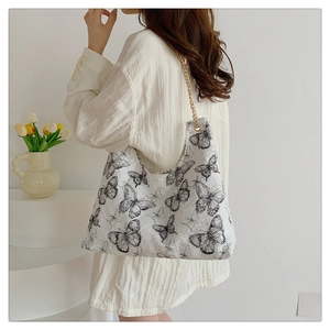 Detailed texture of white canvas bag with black butterfly prints and gold chain strap