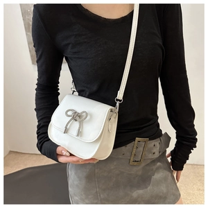 Close-up of white patent leather crossbody bag with a sparkling rhinestone bow detail