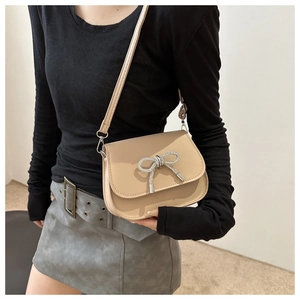 Detail of a beige bow crossbody bag featuring a rhinestone butterfly buckle and PU leather