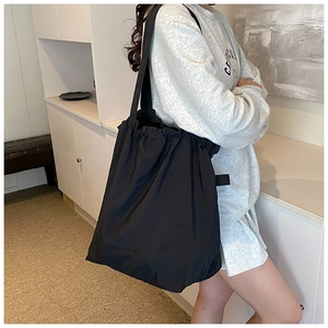 Side view of a large black drawstring tote bag worn by a model in a minimalist interior