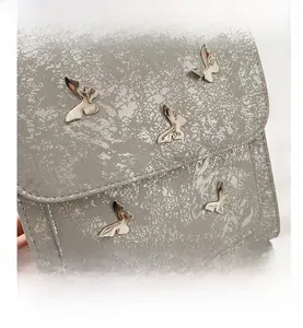 Macro detail of textured faux leather shoulder bag with vintage metallic butterfly buckles