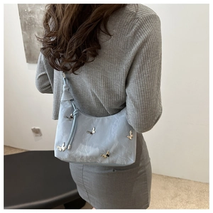 Detail of light blue textured shoulder bag with silver butterfly metal embellishments