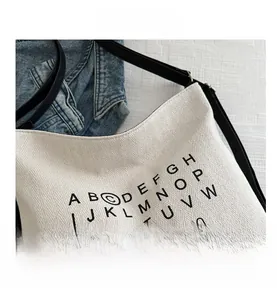 Detailed macro view of white canvas hobo bag with black letter patterns and thin straps