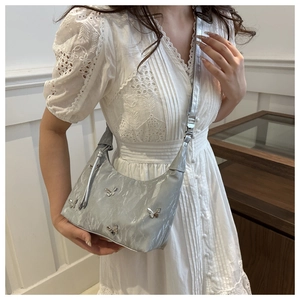 Silver metallic dumpling bag with butterfly charms worn by a model in a white lace dress