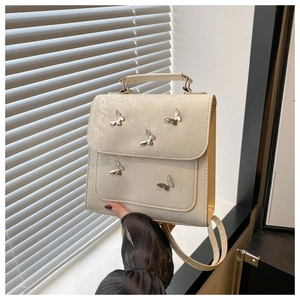 Detailed shot of cream PU leather backpack featuring five silver metal butterfly accents