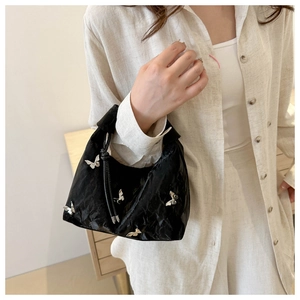 Détail du sac plissé noir avec breloques papillon argentées et bandoulière à nœuds