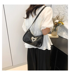 Detail of a black shiny patent leather underarm bag featuring a crystal heart buckle