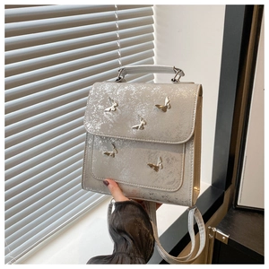 Detail of silver metallic crossbody bag featuring 3D butterfly ornaments and top handle