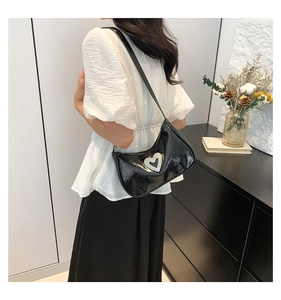 Detail of a black patent leather shoulder bag featuring a sparkling rhinestone heart buckle