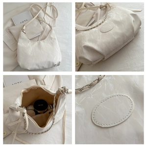 Detail view of large beige tote bag with pleated texture and silver metal chain strap