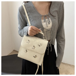 Detail of cream crossbody bag with silver butterfly accents and adjustable shoulder strap