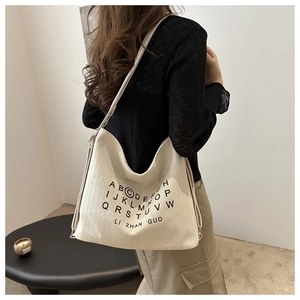 Detail of a large hobo bag in cream woven fabric with letter print on the shoulder