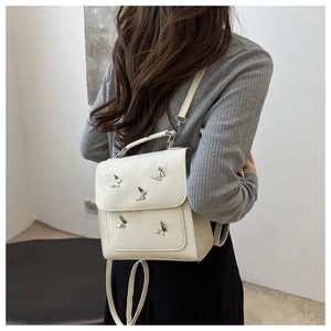 Rear view of model wearing a creamy white butterfly-shaped backpack with metallic details