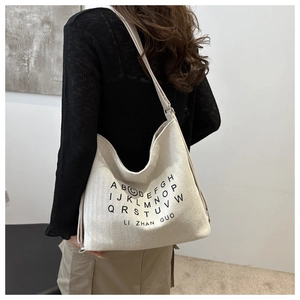 Detail of a beige canvas hobo bag with black alphabet print and textured fabric weave
