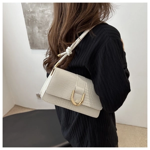 Détail macro du sac crème gaufré crocodile avec boucle dorée en U et bandoulière nouée