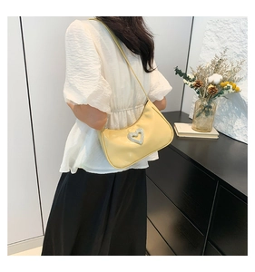 Model wearing a bright yellow patent leather underarm bag with a rhinestone heart buckle