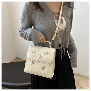 Detail view of cream butterfly handbag with silver metallic charms worn by a model